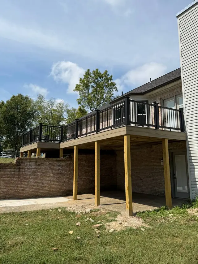 Finished elevated deck with pressure treated support posts, fascia and black railings viewed from the yard Finished elevated deck with pressure treated support posts, fascia and black railings viewed from the yard