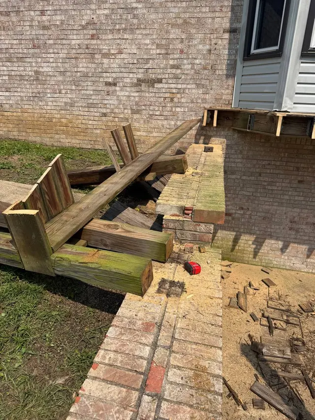 Cut sections of old deck posts and framing during demolition beside the brick retaining wall Cut sections of old deck posts and framing during demolition beside the brick retaining wall