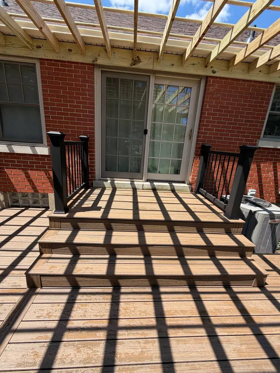 Composite stairs leading to a brick home beneath a pergola