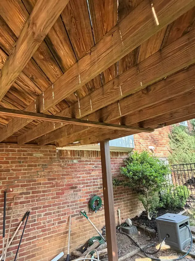 Old wood joists and decking viewed from beneath the upper deck beside the brick home
