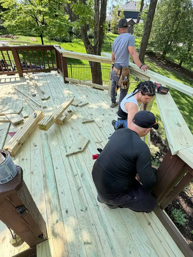 Three crew members assembling new wood railing sections on the middle deck, with materials and offcuts nearby
