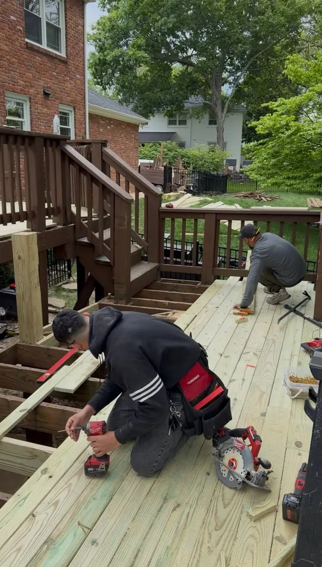Two crew members fastening pressure treated boards on the repaired middle-level frame before the new railing sections are built