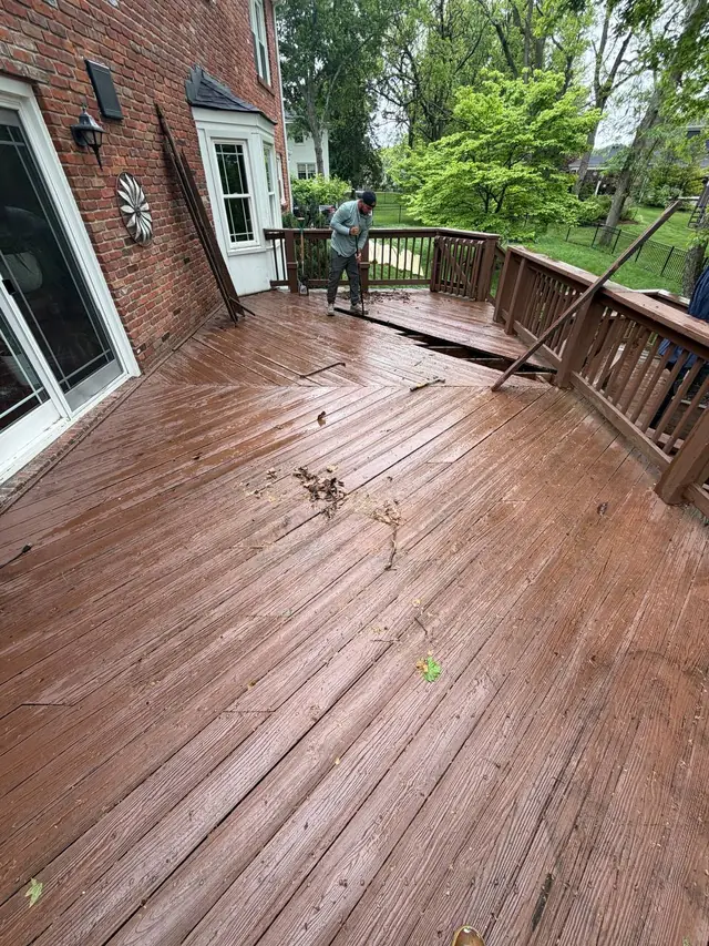 Crew member prying up old upper-level deck boards, exposing the joists beneath