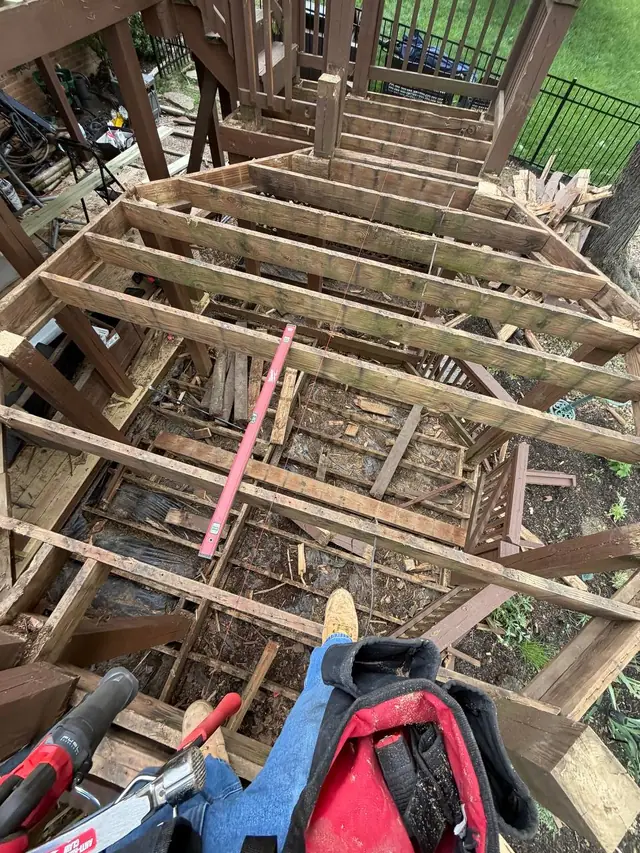 Old middle-level joists exposed after deck board removal, with a level, string line and the open lower deck beneath