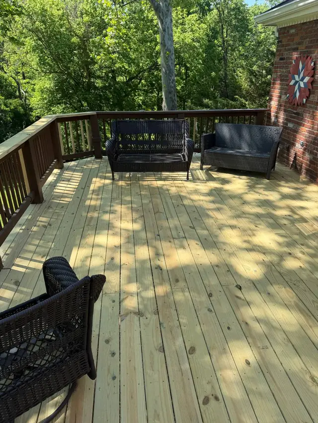 New upper-deck boards and completed top rails around a furnished seating area beside the brick wall