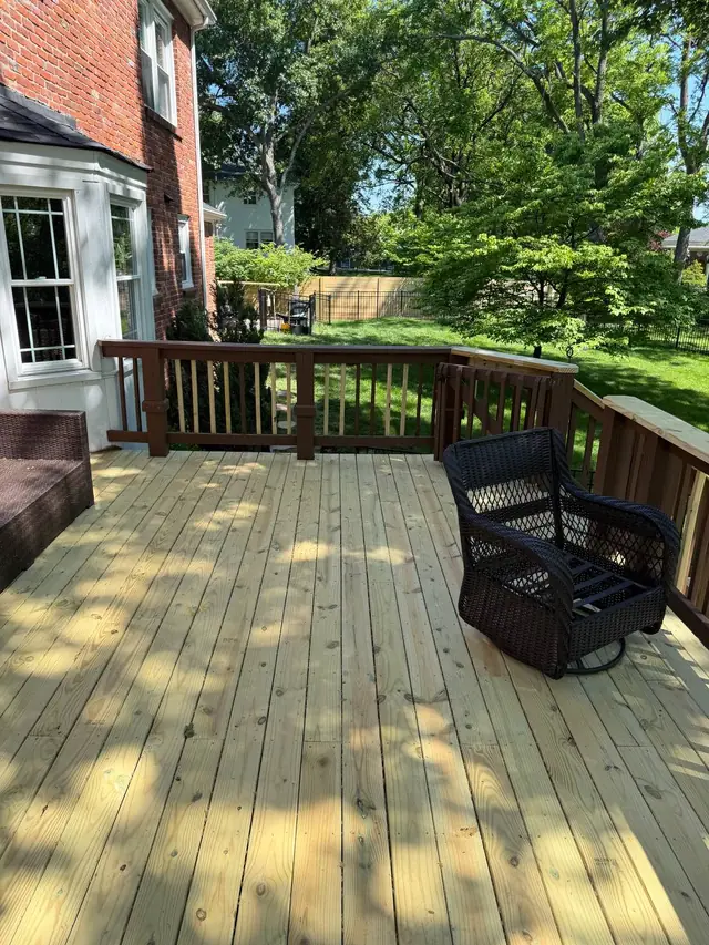 Fresh upper-level decking and selected new wood balusters beside a dark wicker chair and the brick bay window
