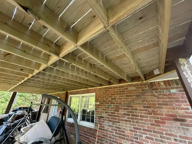 New upper-level joists, blocking and deck boards above the retained perimeter framing beside the brick house