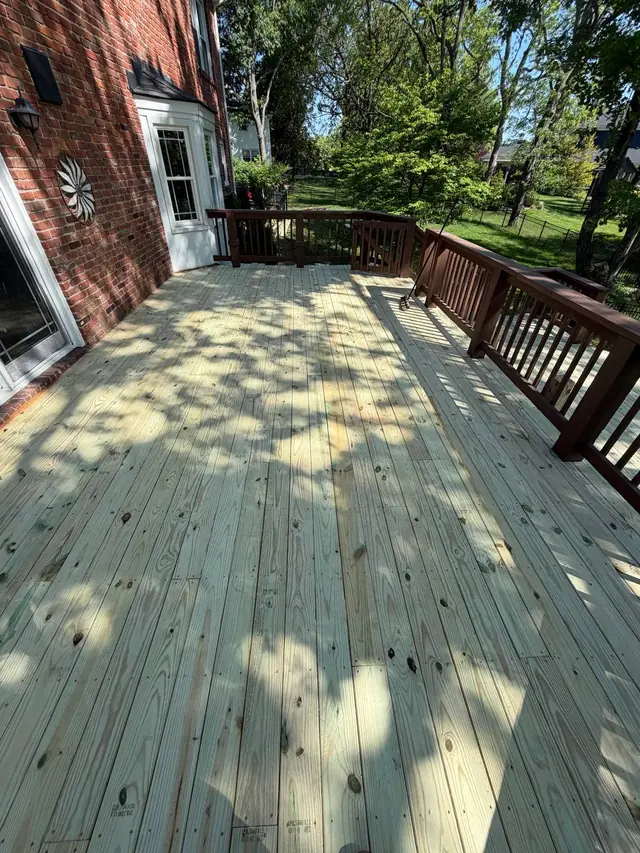 Fresh upper-level deck boards before the remaining top rail and baluster replacements, with a broom against the railing